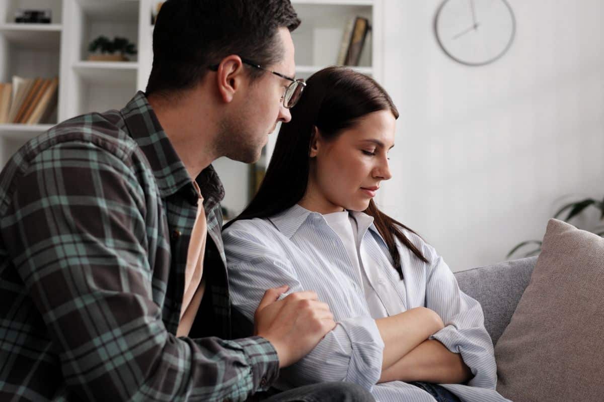 Man apologizing to woman; sitting on couch. 