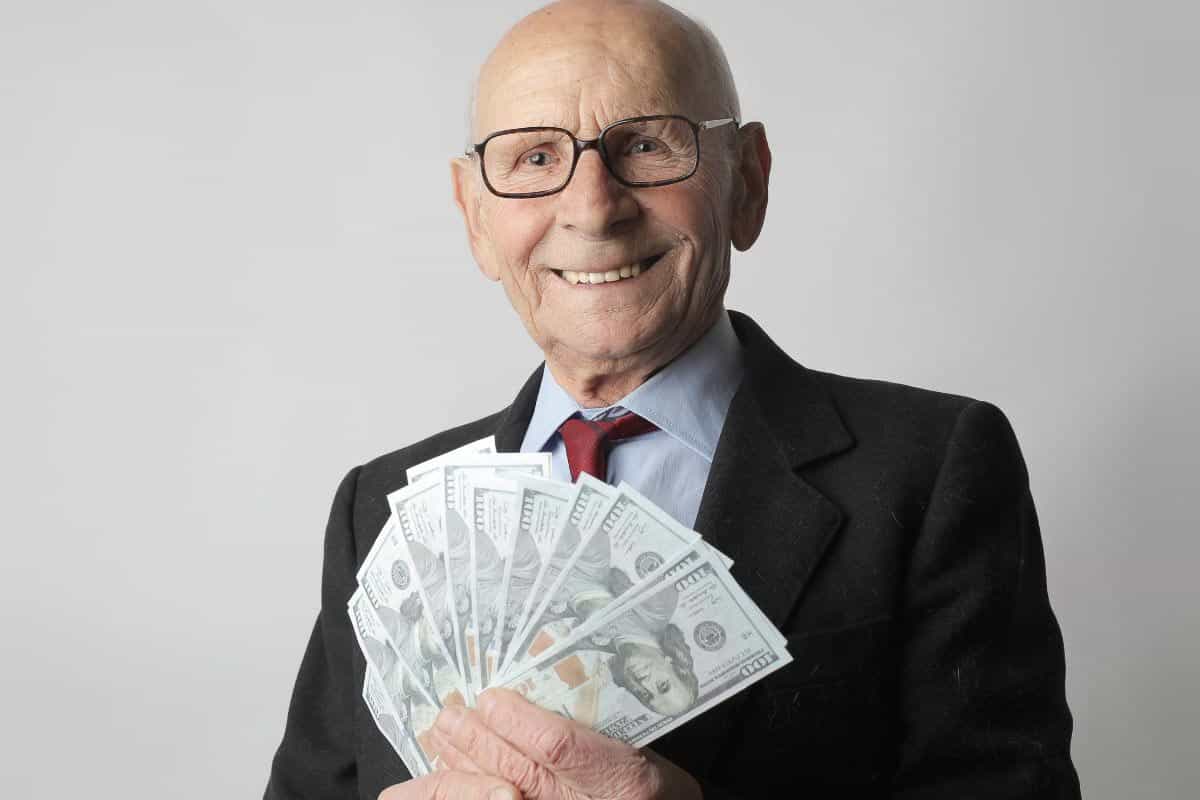 Man in dark suit holds fan of paper bills. 