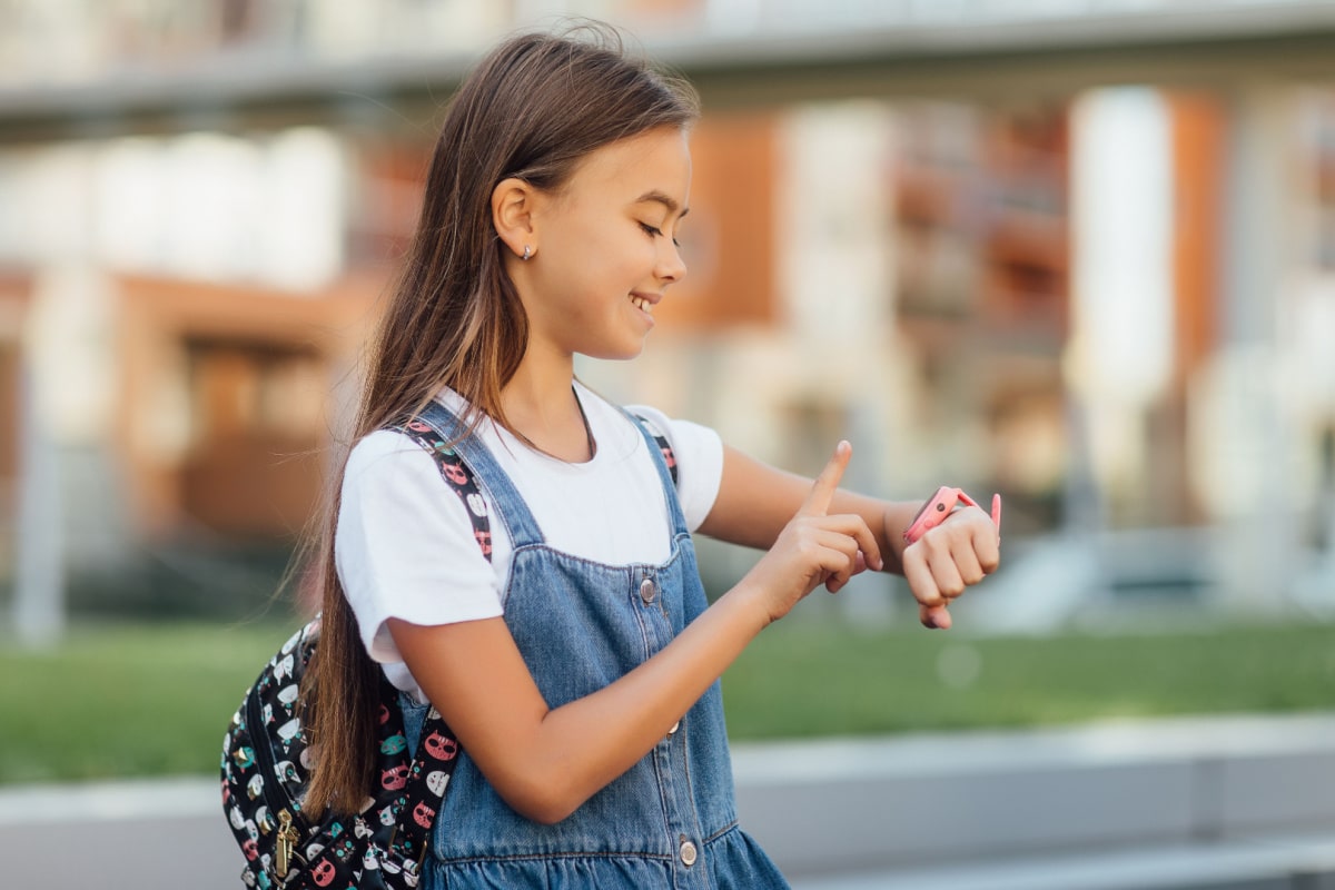 Technology for children, a girl wearing jeans dress uses a smartwatch on fresh air. Lifestyle.