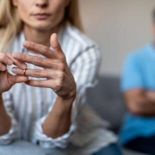 Unhappy middle aged european lady takes off ring, ignoring man during quarrel in living room interior, cropped. Relationship problems, divorce, scandal and breakup, emotions at home due covid-19.