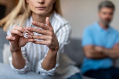 Unhappy middle aged european lady takes off ring, ignoring man during quarrel in living room interior, cropped. Relationship problems, divorce, scandal and breakup, emotions at home due covid-19.