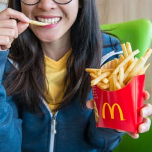 Woman holding and eating french fries in McDonald's restaurant.