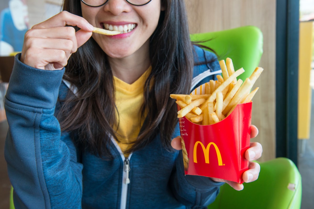 Woman holding and eating french fries in McDonald's restaurant.