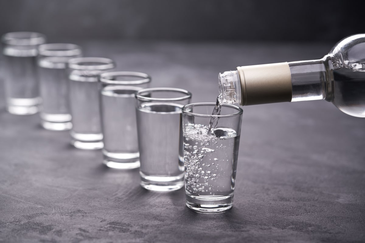 Pouring vodka into the glass on a black background, selective focus.