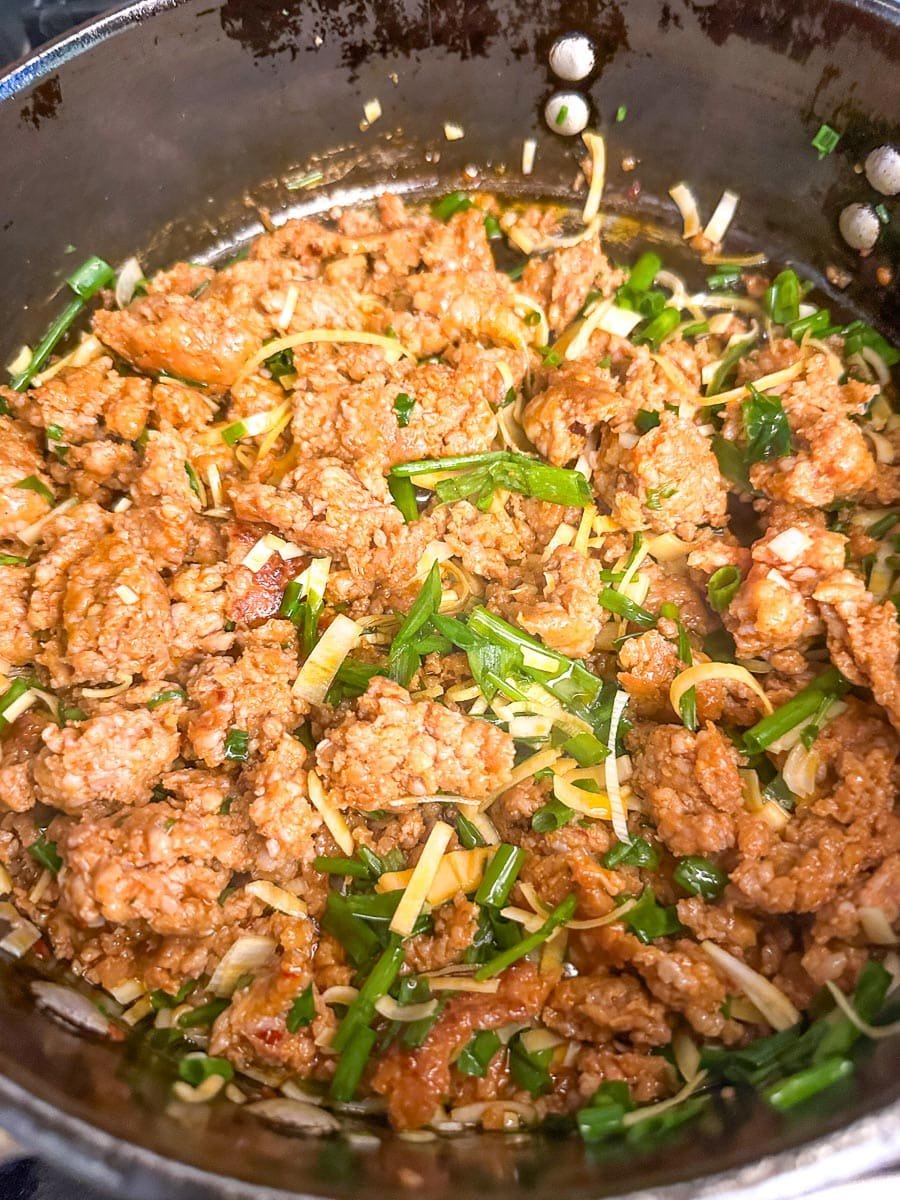 browning sausage in pan with scallion greens and leeks.