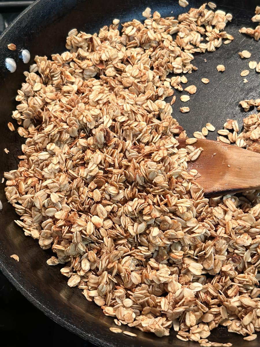 close-up of toasted granola in pan with wooden spoon.