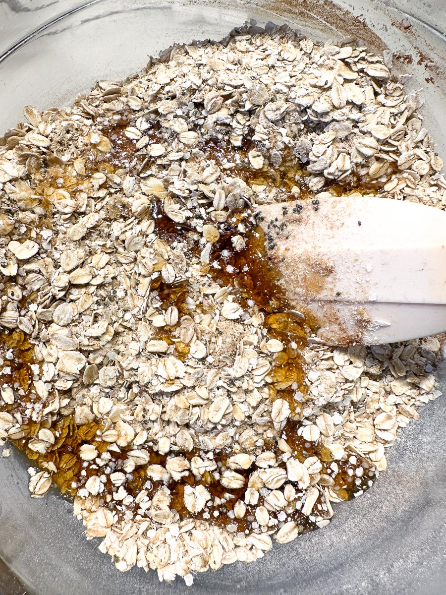 dry and wet Ingredients for low FODMAP high protein Quinoa and oat granola in glass bowl with spatula.
