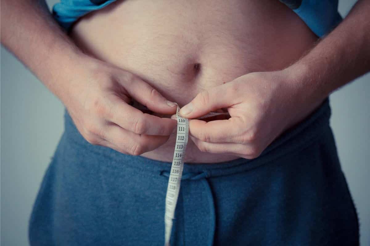 man holding measuring tape around belly. 