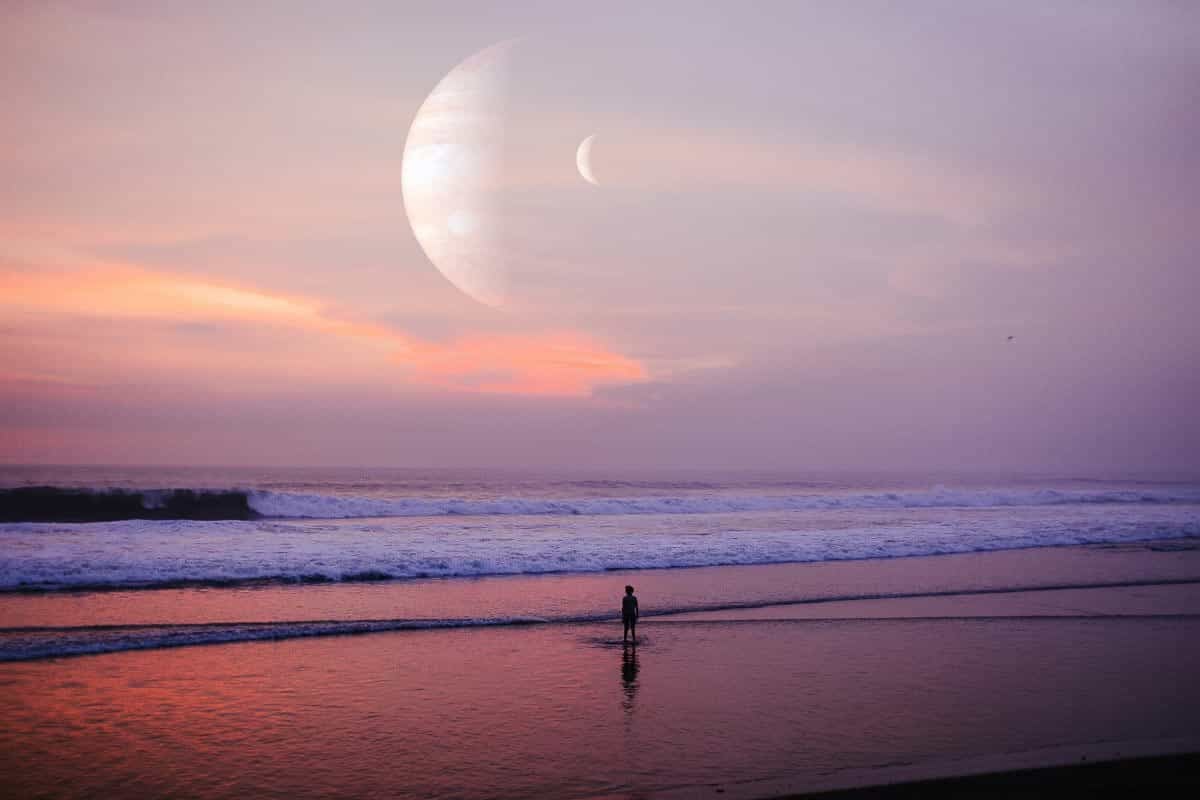 person on beach with sunset and planets in sky.