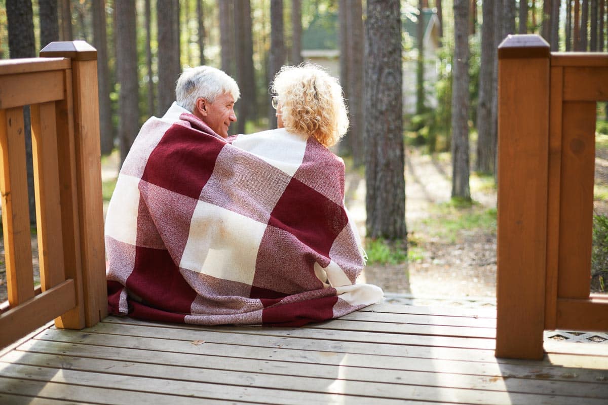 couple sitting on porch wrapped in blanket.