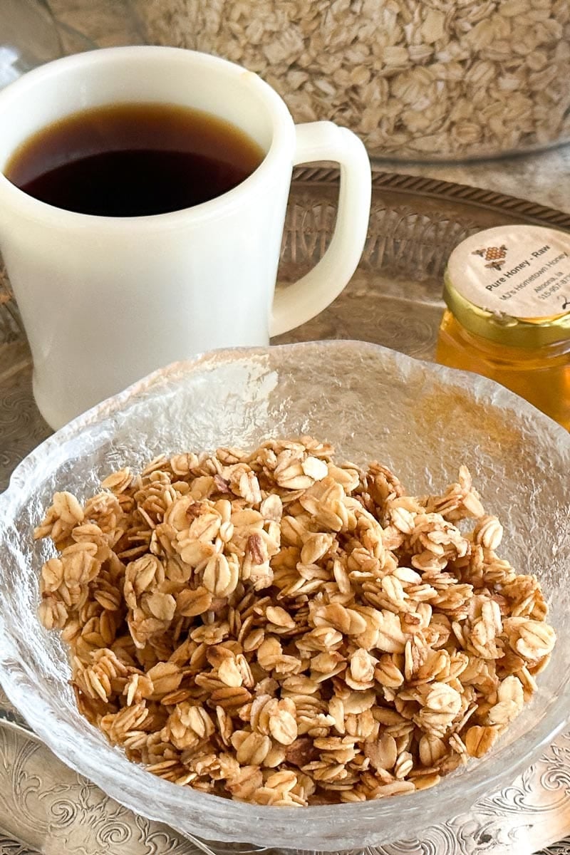 vertical image of Low FODMAP 5-Minute Skillet Honey Butter Granola in glass bowl on silver platter