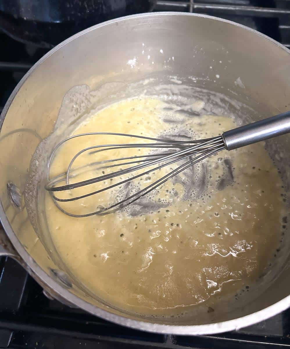 whisking flour into butter to make roux in pot.