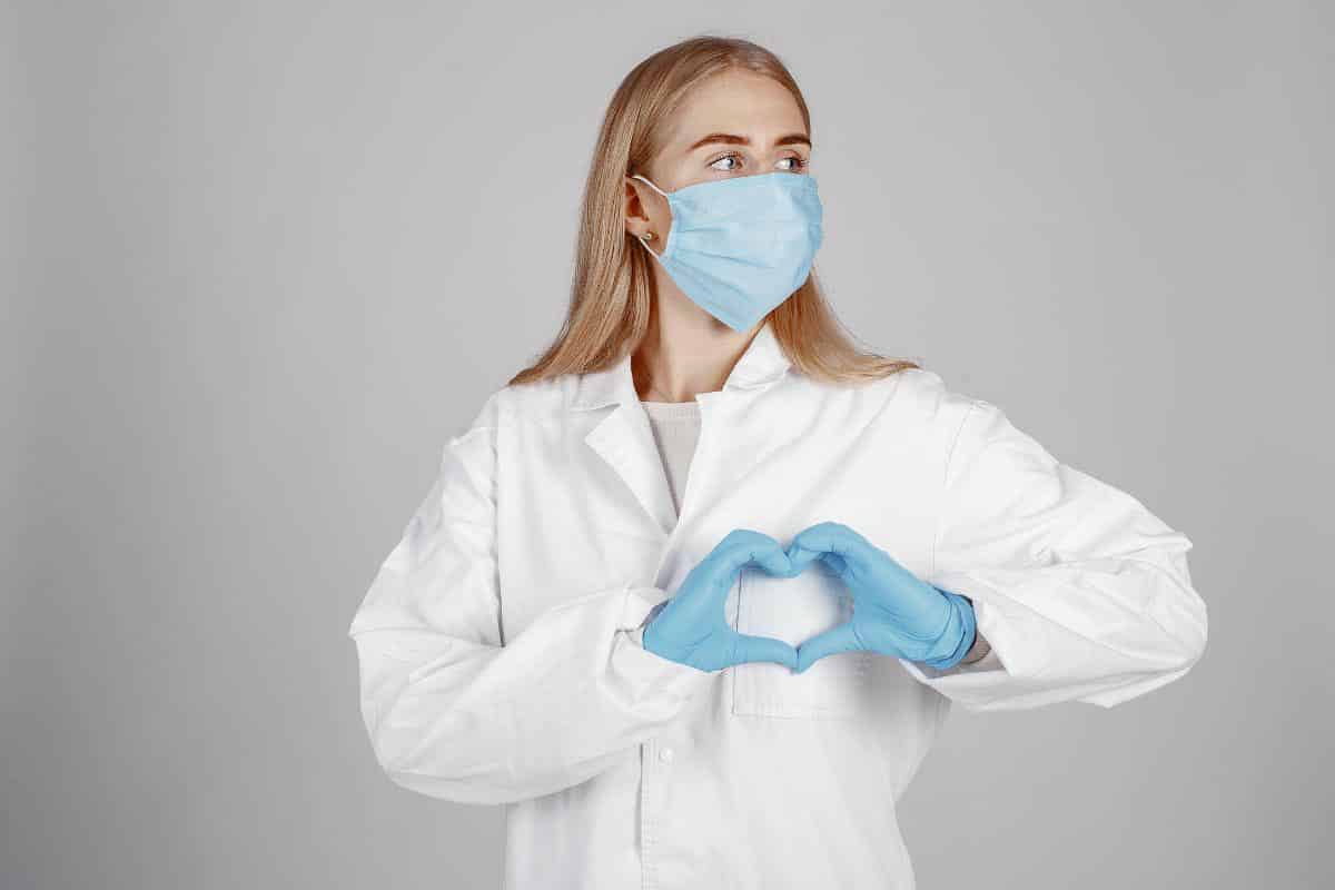 woman in lab coat showing heart with hands. 