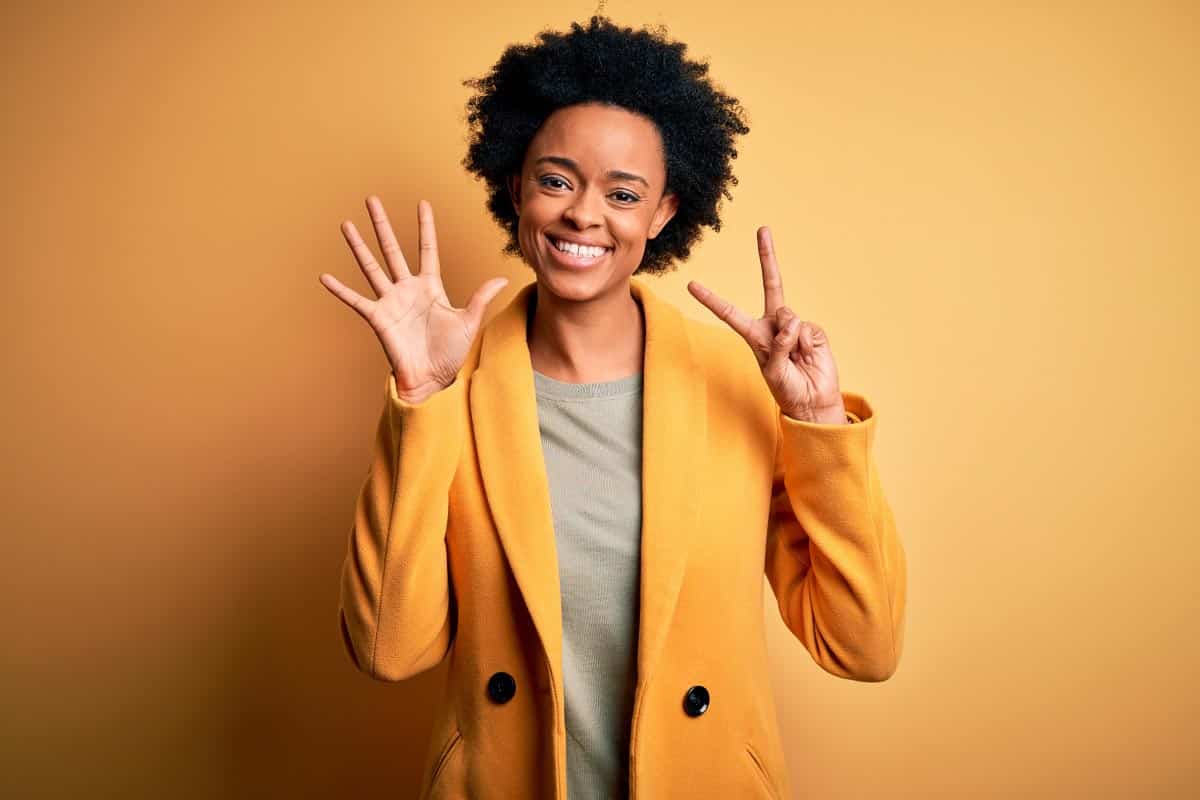 woman in yellow holding up 7 fingers. Shutterstock_1762290215.