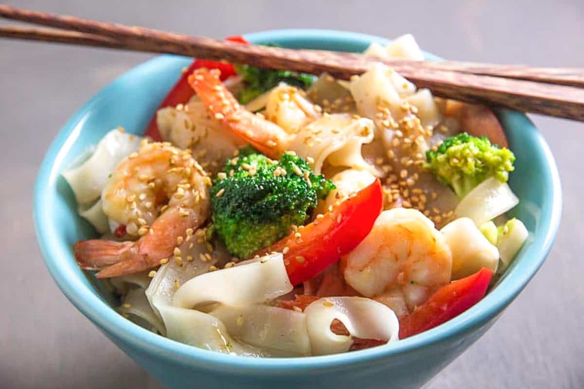 aqua-bowl-of-low-FODMAP-shrimp-and-broccoli-with-noodles-chopsticks-on-top-of-edge-of-bowl.