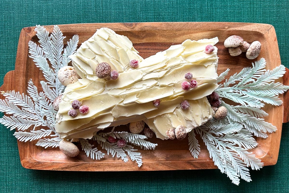 Low FODMAP Gingerbread Buche de Noel on wooden platter with fake frosted pine boughs.