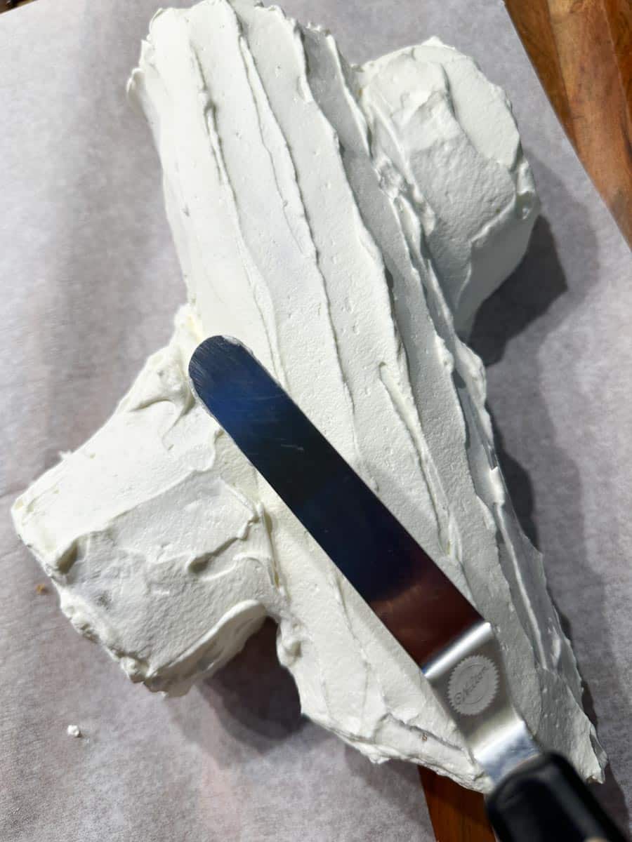 Using small icing spatula to create bark texture in whipped topping of buche de noel.