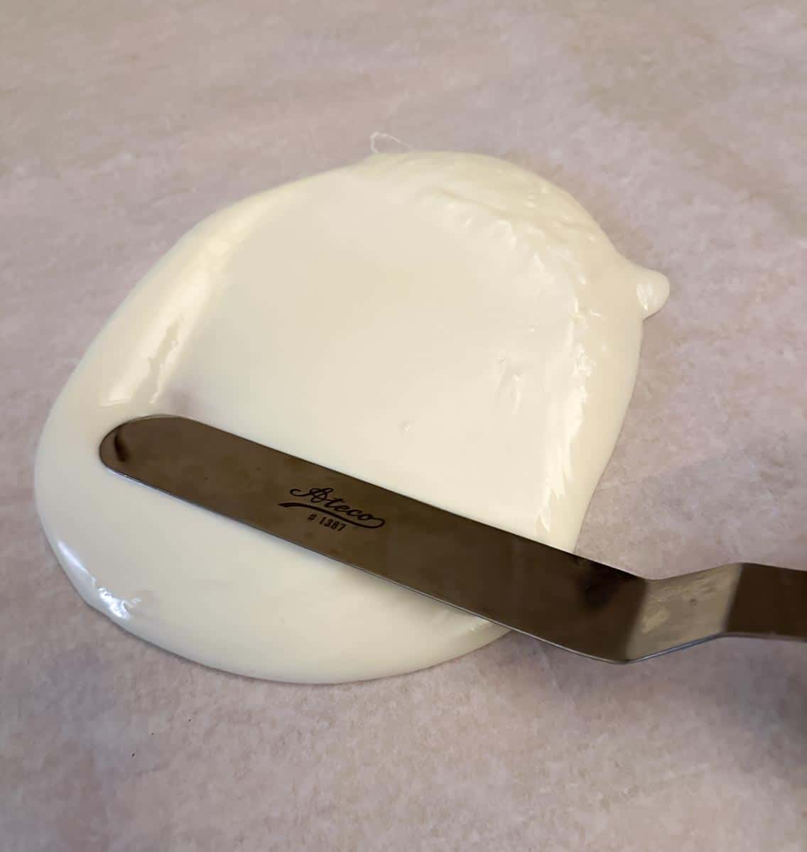small offet spatula spreading white chocolate on parchment paper.