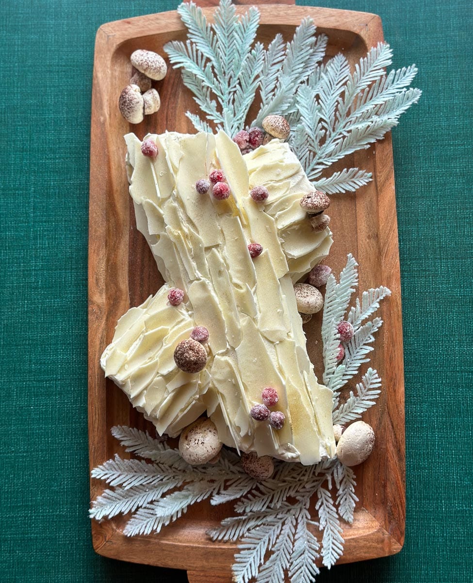 vertical image of Low FODMAP Gingerbread Buche de Noel on wooden platter with fake frosted pine boughs.