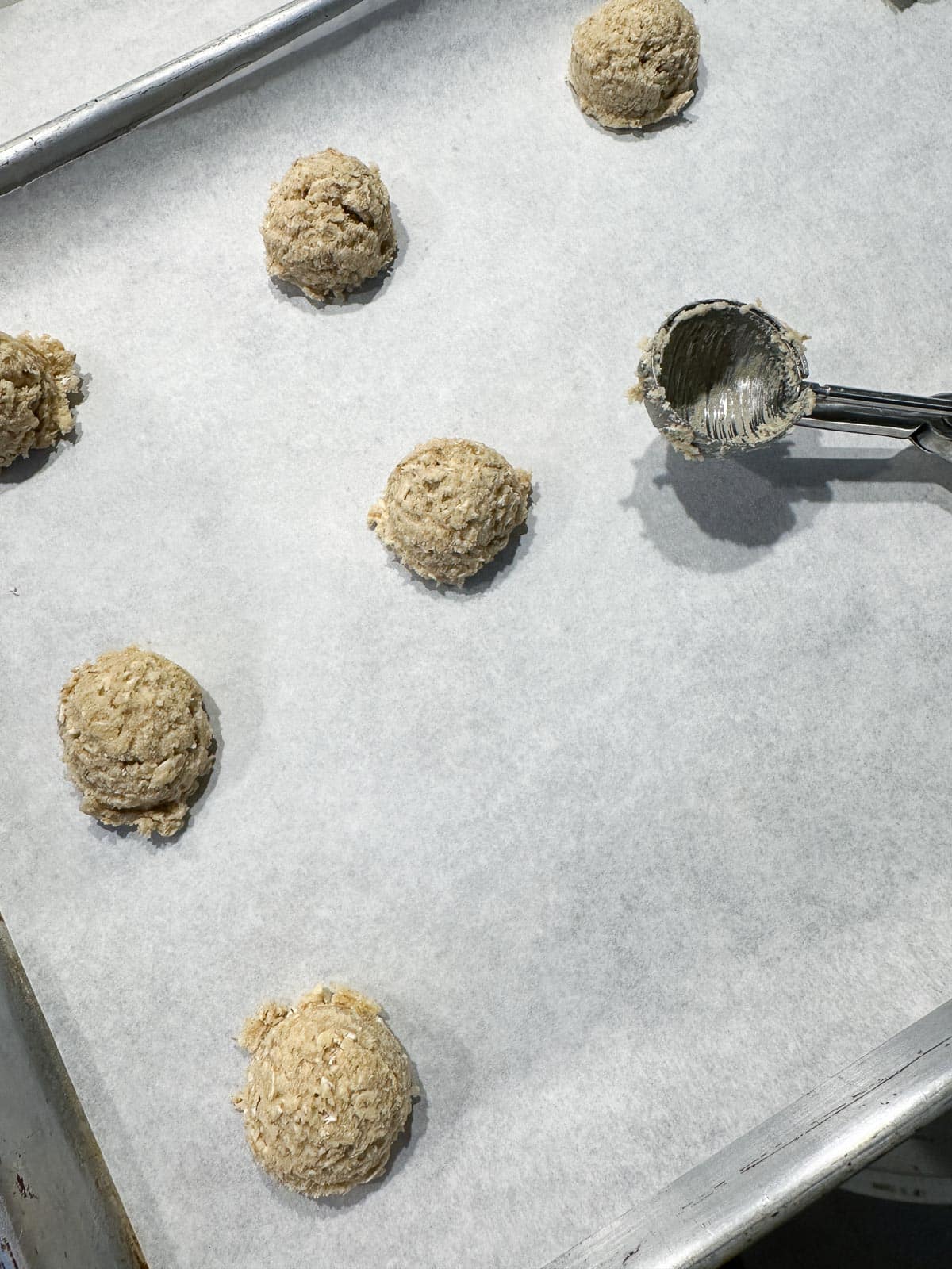 doling oatmeal cookies out on pan with cookie scoop.