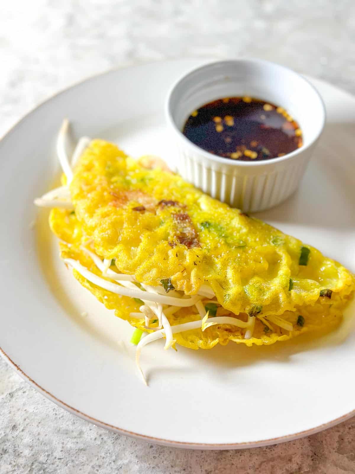 Closeup Low FODMAP Vietnamese Pancake on white plate with Nuoc Cham Dipping Sauce.