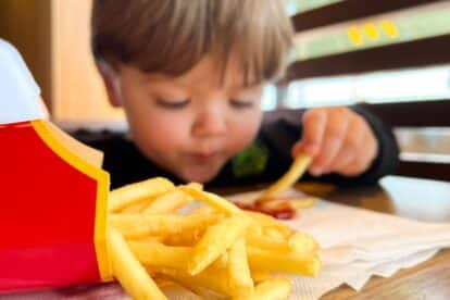 A little boy, caucasian child eating McDonald's fries with ketchup inside McDonald's restaurant. Unhealthy fast food eaten by a kid.