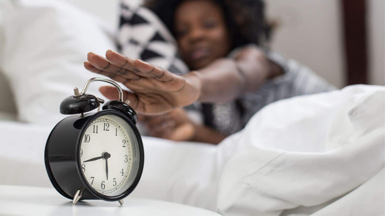 woman waking up in bed and turning her alarm clock off