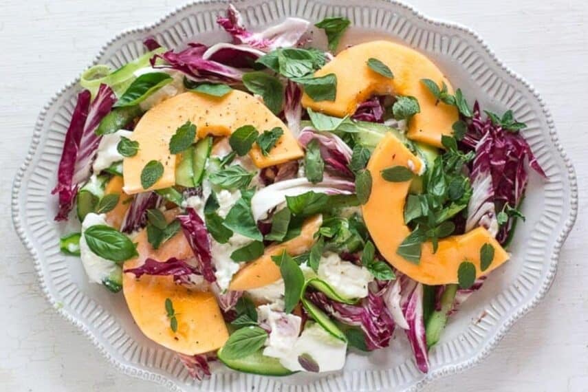 cantaloupe-cucumber-and-burrata-salad-with-herbs-on-a-white-platter-and-white-wooden-surface.