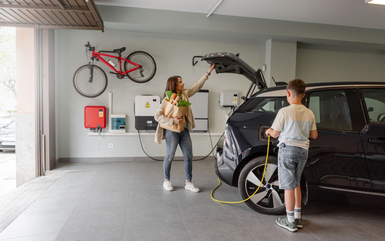 Son plugs EV charger from charging station to electric vehicle in private home while mother takes groceries from the car on daytime. Sustainable Alternative Lifestyle. Horizontal copy-space.