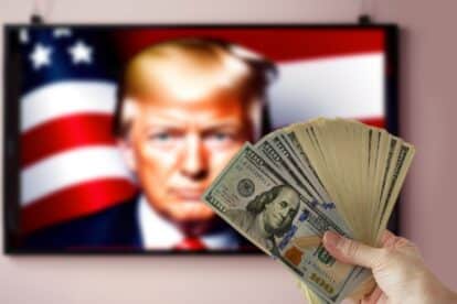 Washington, USA - September 16 2024: hand holding pile of money cash on Donald Trump portrait on TV background. US election 2024.