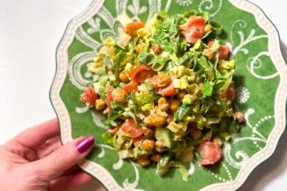 closeup Low FODMAP Crispy Chickpea Chopped Salad with Lemon Tahini Dressing hand holding plate.