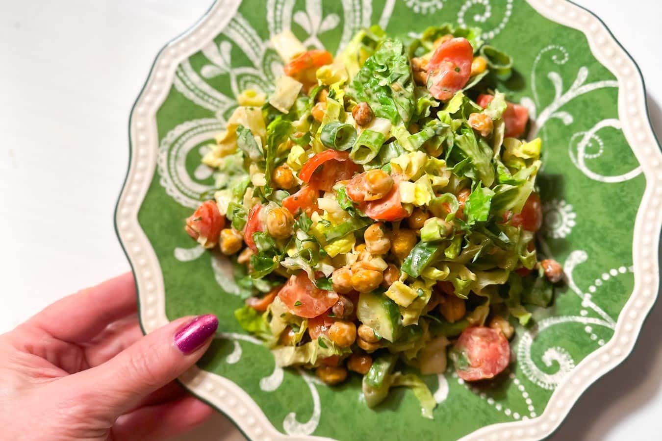 closeup Low FODMAP Crispy Chickpea Chopped Salad with Lemon Tahini Dressing hand holding plate.