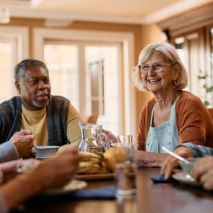 Group of senior friends communicating while eating lunch in nursing home. Focus is on happy woman.