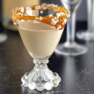 Low FODMAP Salted Caramel Liqueur in glass with caramel and coarse salt.