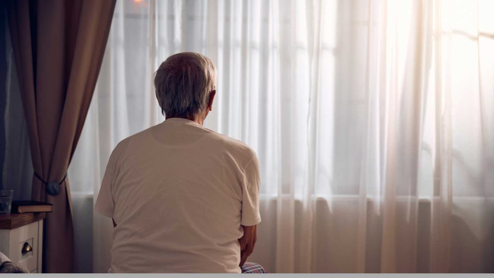 Rear view of senior man sitting alone in bedroom. Copy space.