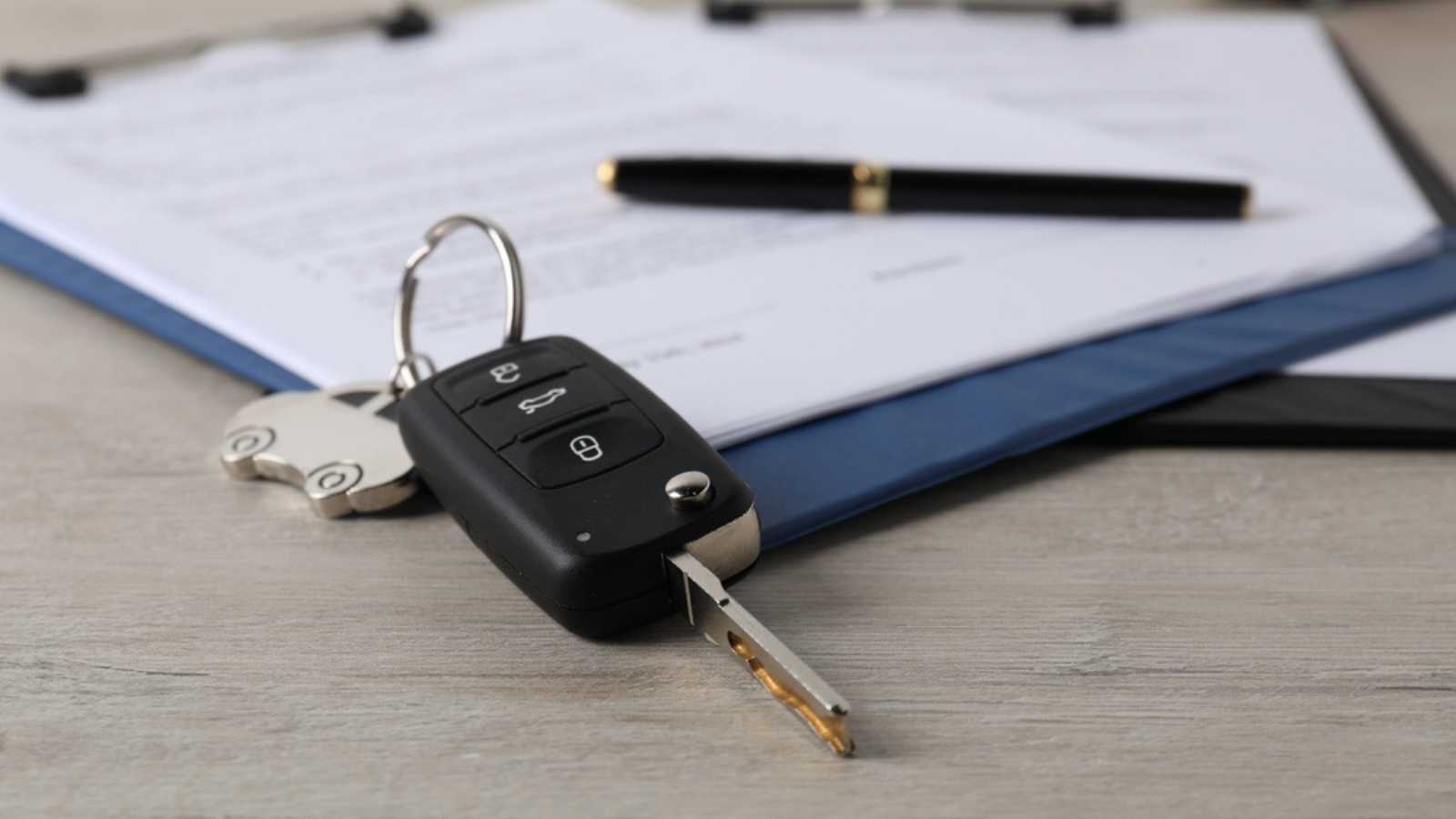 Car key and purchase agreement on wooden table, closeup. Buying auto finance financing