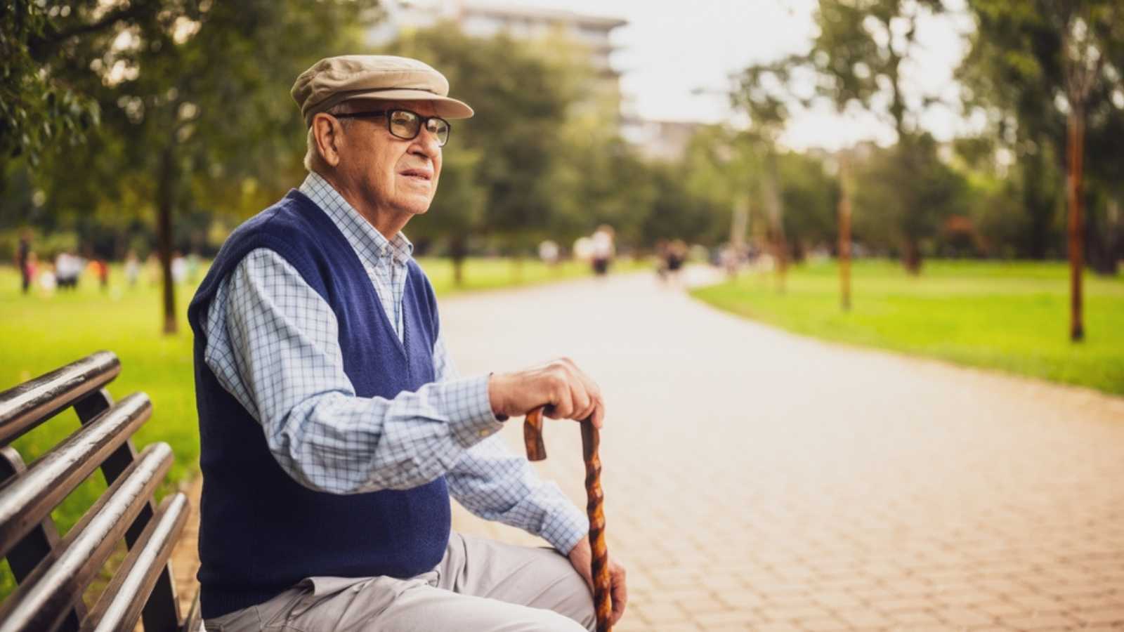 Portrait of lonely senior man in park. He is sitting on bench on autumn day.