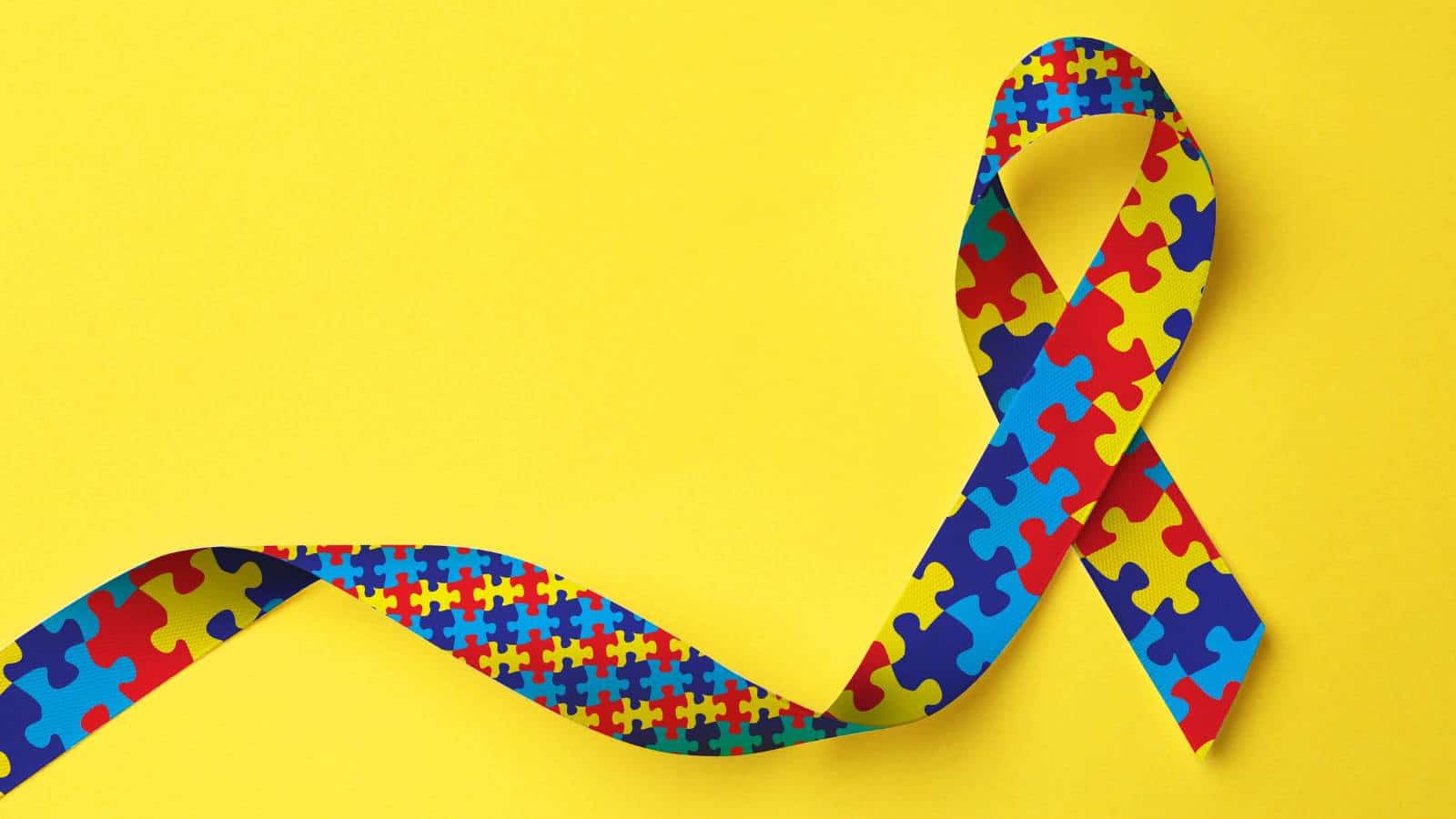 World Autism Awareness Day. Colorful puzzle ribbon on yellow background, top view