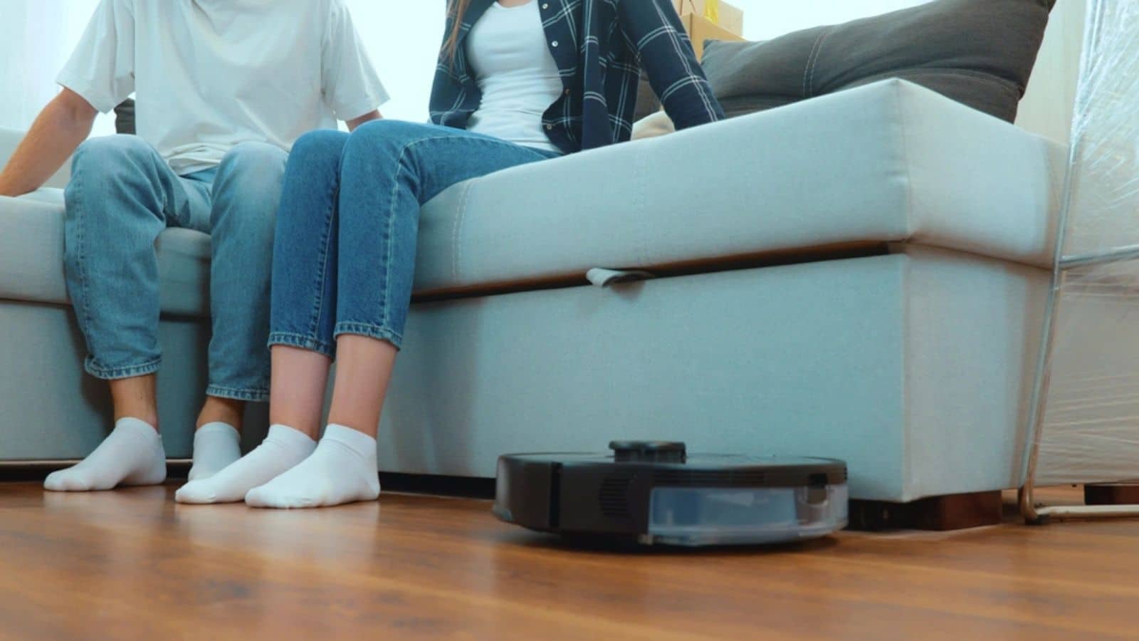 Couple sitting on sofa as robot vacuum cleaner cleans home