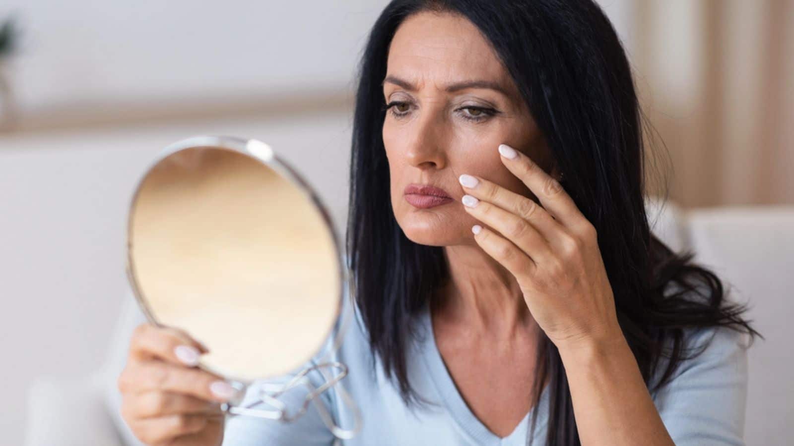 Sad woman touching face and looking in mirror